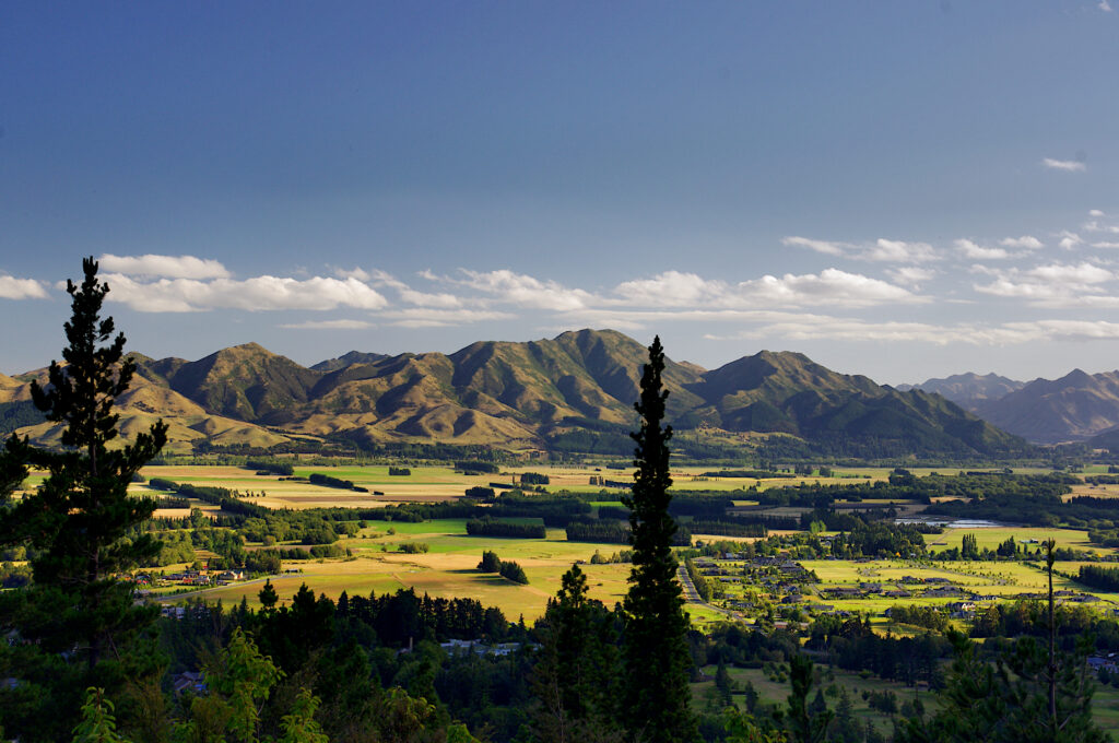 Sunlit valley with green hills distant mountains scattered houses and clear blue sky wallpaper background