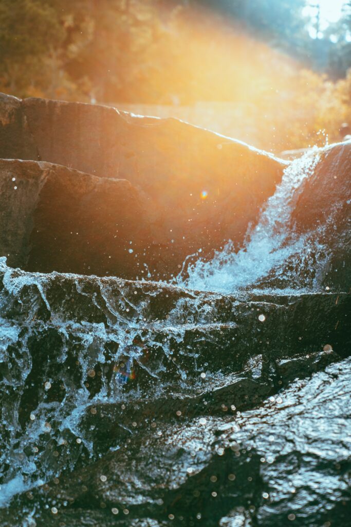Sunlit water flowing over dark rocks with glowing flares vibrant natural wallpaper background