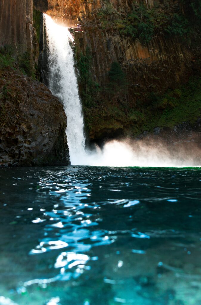 Waterfall cascading over rocky cliffs into clear blue water under bright sunlight scenic background Wallpaper