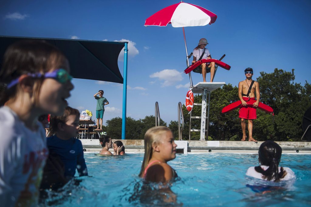 Sunny lifeguard watching children swim in blue pool water under red and white umbrella Wallpaper