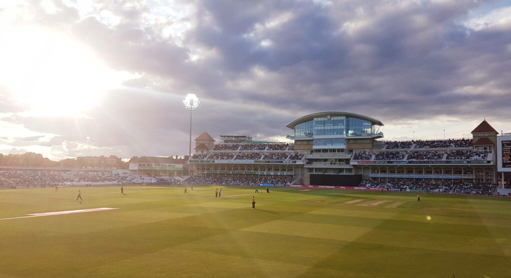 Sunlit Splendor: Majestic Cricket Stadium amidst Lush Greenery Wallpaper