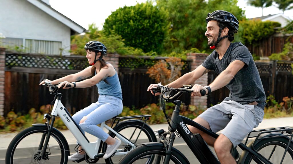 Two riders on modern electric bikes enjoying a sunny suburban day with green natural scenery Wallpaper