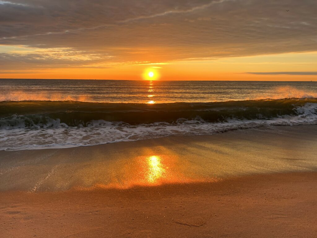 Sunrise beach wallpaper with golden sunlight reflecting on waves and wet sand in warm hues