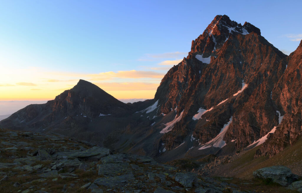 Sunrise over rugged mountain slopes with snow patches clear skies tranquil natural landscape Wallpaper