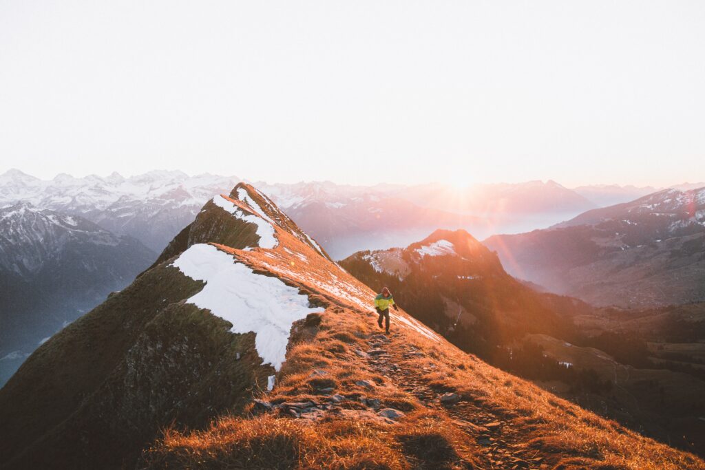 Tourist hiking rugged mountain ridge at sunrise with snow patches and dramatic peaks background Wallpaper