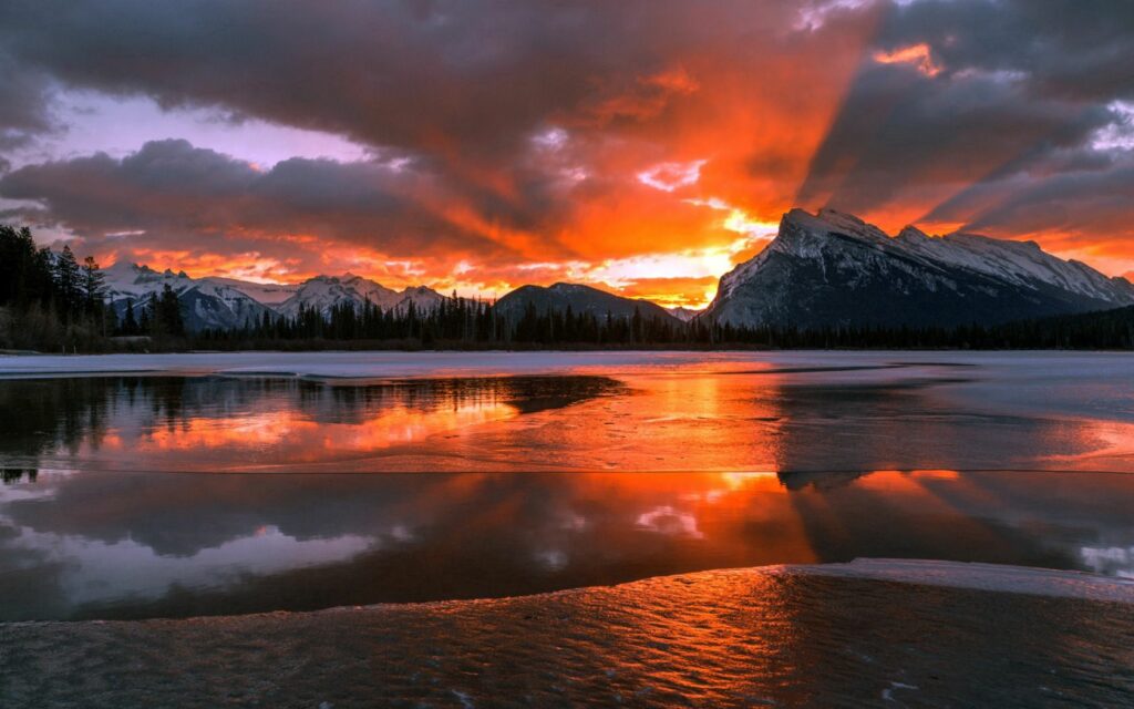 Sunrise over Banff National Park with vibrant orange skies and snowy mountains reflected on lake Wallpaper