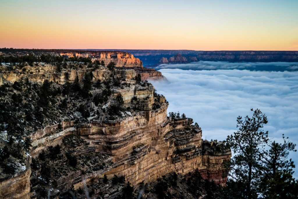 Sunrise over rugged cliff and ridge above sea of clouds with warm light on rocky peaks wallpaper