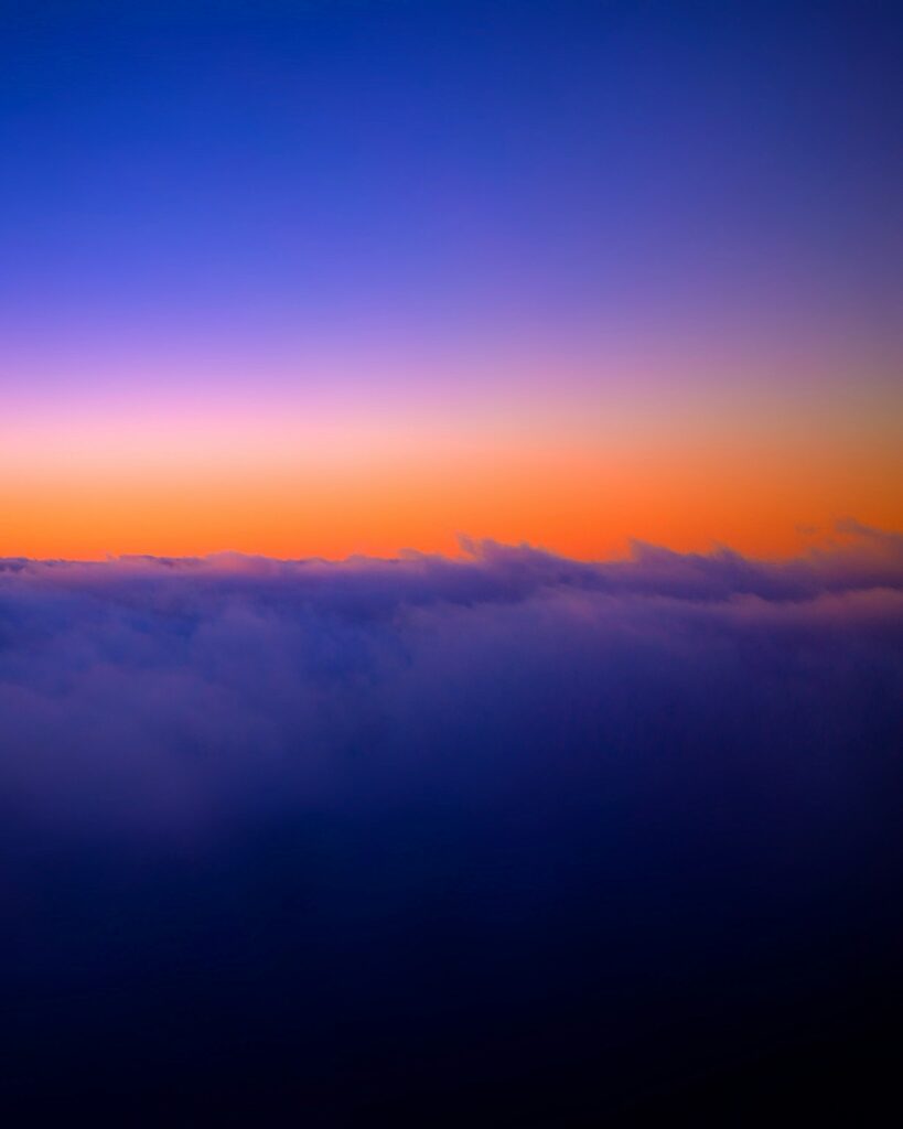 Sunset sky above clouds with deep blue orange and violet twilight hues peaceful wallpaper background