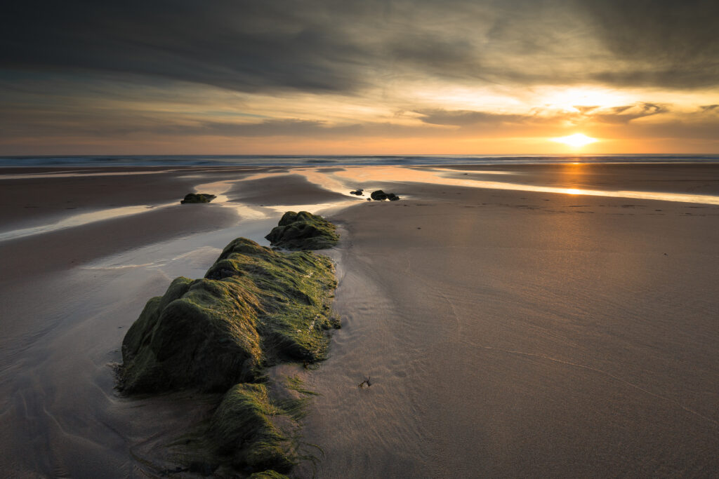 Aerial view of sandy beach at sunset with mossy rocks golden sky and tranquil streams wallpaper