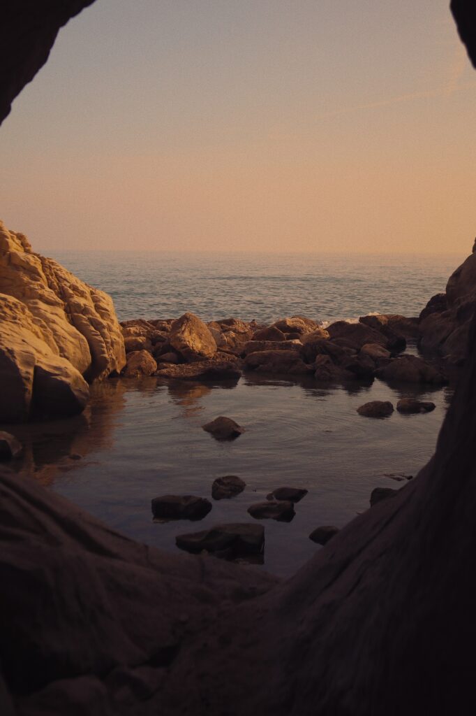 Sunset over tranquil bay with rugged rocks smooth stones and golden light on calm sea horizon Wallpaper