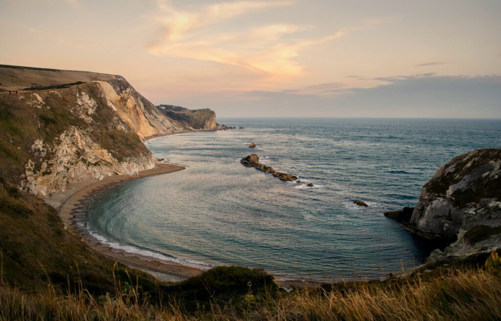 Sunset over serene bay with rugged cliffs and gentle waves in a peaceful coastal landscape wallpaper