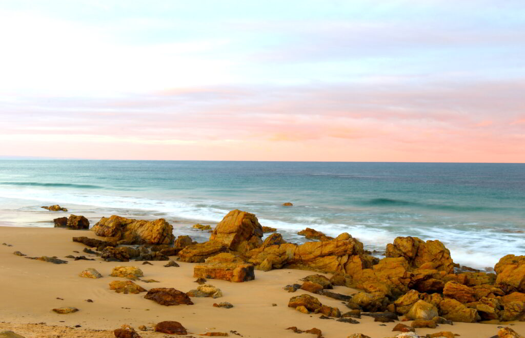 Tranquil beach wallpaper with golden sand rugged stones gentle waves and pastel sunset sky