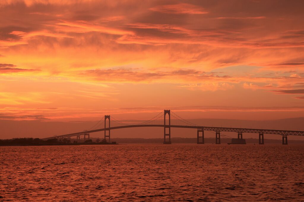 Striking bridge over calm sea at vibrant orange and gold sunset reflecting on water horizon view Wallpaper