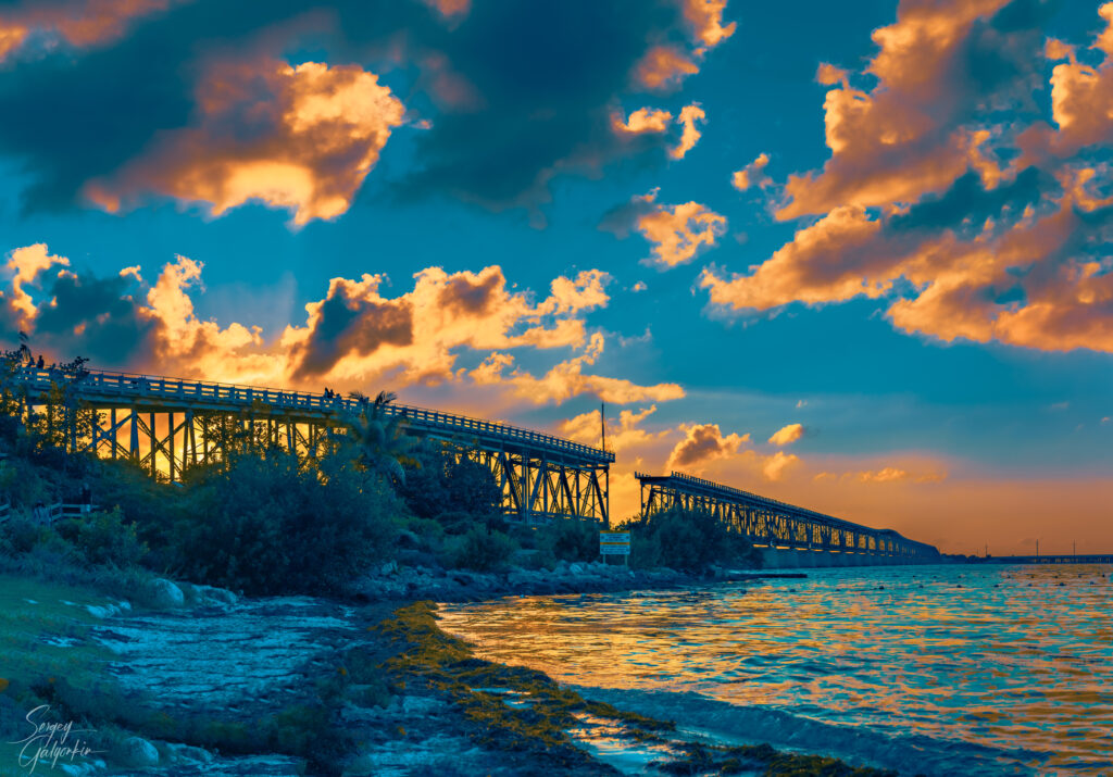 Scenic long bridge over calm water at sunset with golden clouds vibrant tranquil landscape Wallpaper