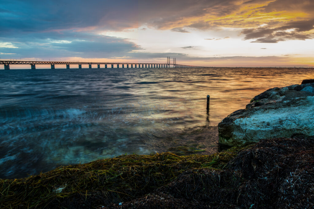 Long bridge over ocean at vibrant sunset with dynamic waves and dramatic coastal clouds wallpaper