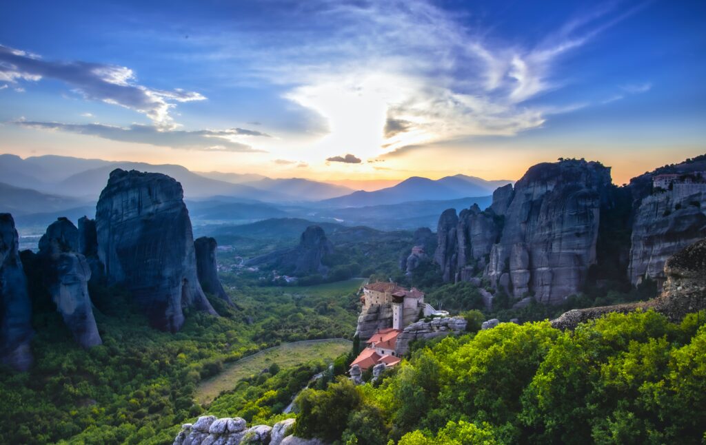 Sunset landscape with rocky cliffs lush valley and distant castle showcasing nature’s grandeur Wallpaper