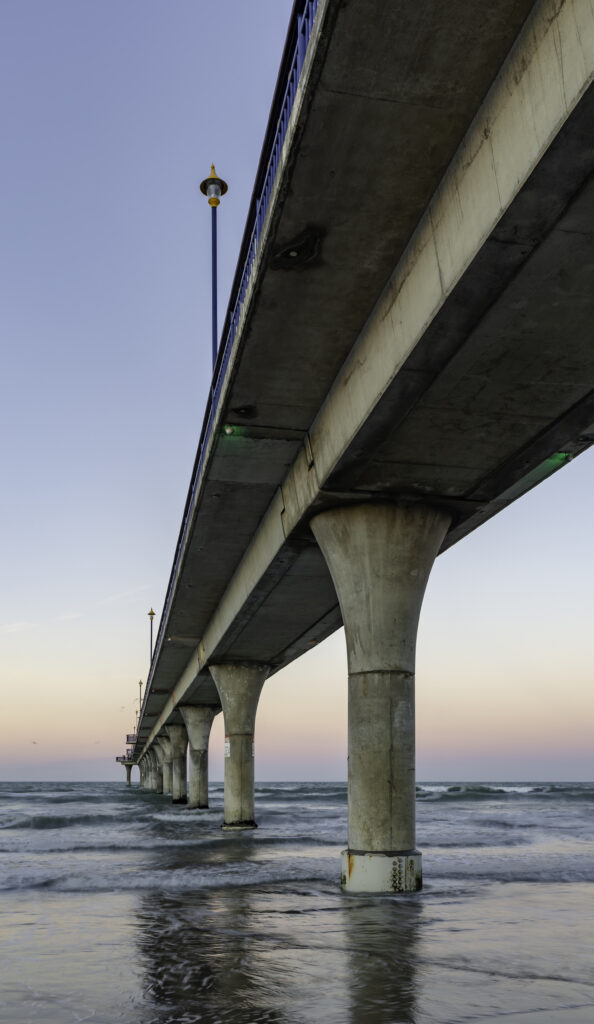 View beneath concrete bridge over calm waves at pastel sunset peaceful coastal wallpaper background