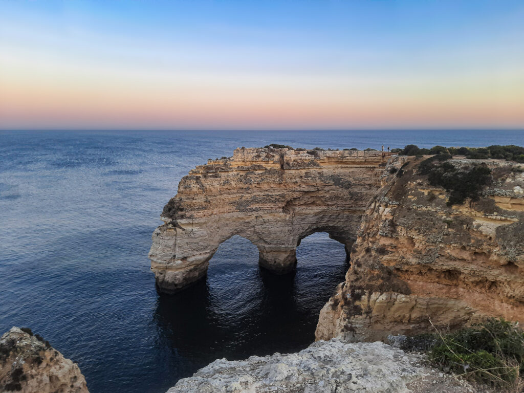 Sunset coastal cliffs with natural rock arches over calm sea and pastel sky wallpaper background
