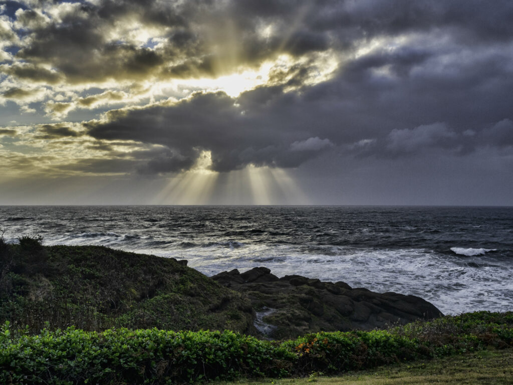 Sunset coastal landscape with dramatic clouds sun rays rolling waves rocky shore vibrant greenery Wallpaper