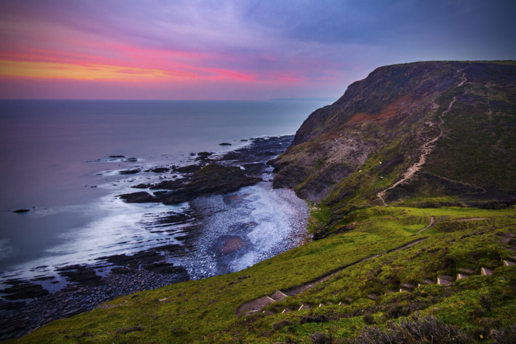 Dramatic coastal sunset with rugged rocks winding path green cliffs vivid pink purple sky wallpaper
