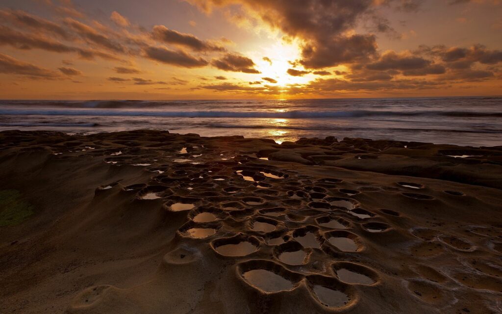 Coastal sunset wallpaper with stony terrain and water-filled hollows by deep blue sea