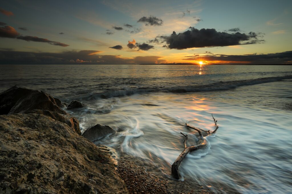 Coastal sunset wallpaper with waves over rocks driftwood warm orange blue hues tranquil sea