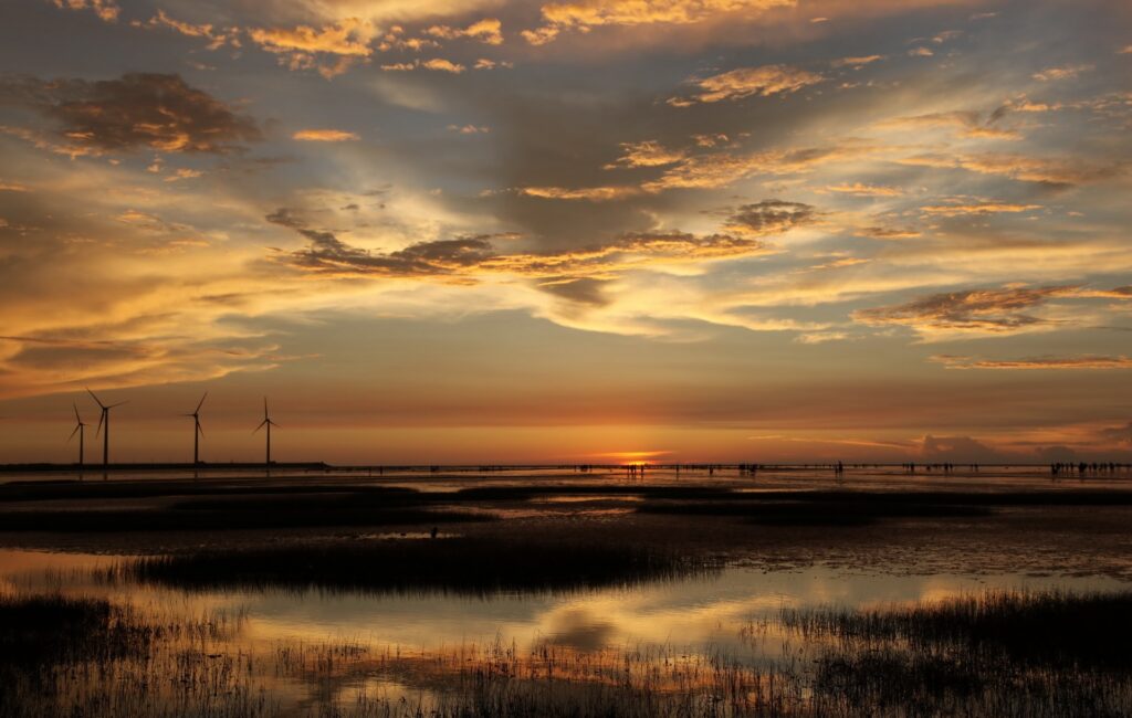 Silhouetted wind turbines at sunset over coastal pools with warm orange and gold sky tones Wallpaper