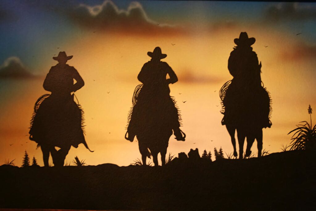 Three cowboys on horseback silhouetted against a warm colorful Western sunset wallpaper background