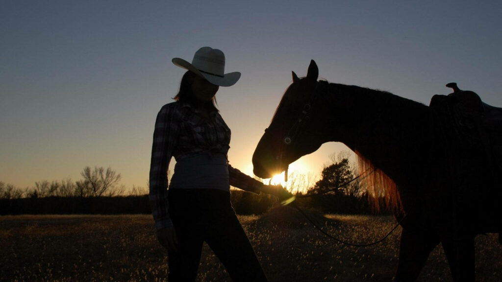 Silhouette of cowgirl with horse in open field at golden sunset capturing Western freedom Wallpaper
