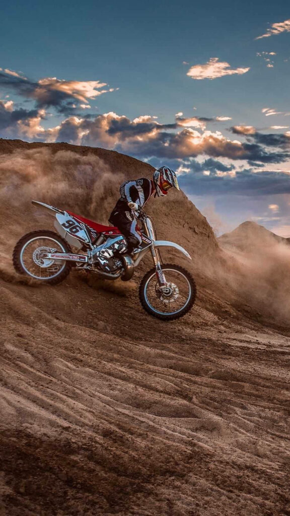 Dirt bike rider speeding through rugged sand at sunset with dust clouds off-road adventure wallpaper