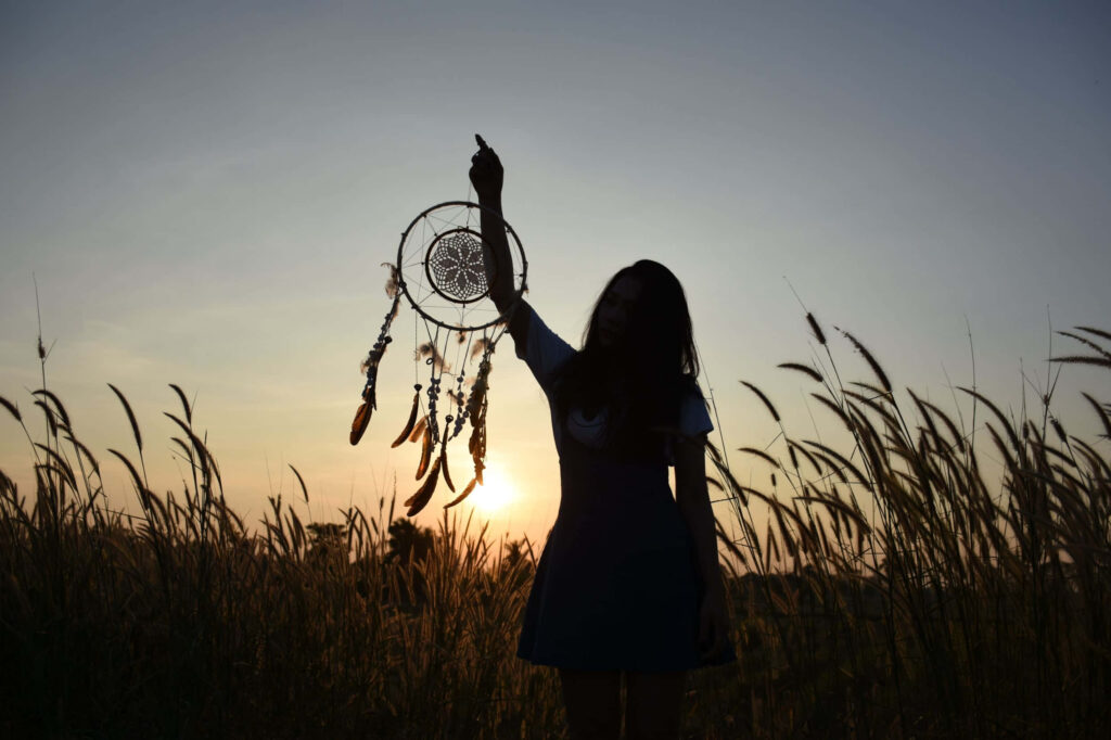 Girl holding dream catcher in sunlit field at sunset symbolizing hope and new beginnings Wallpaper