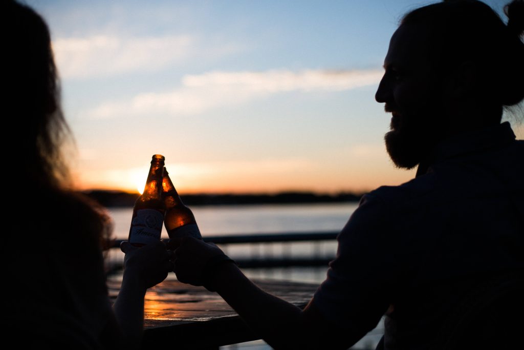 Silhouettes toasting beer bottles at sunset warm golden sky friendship summer wallpaper background