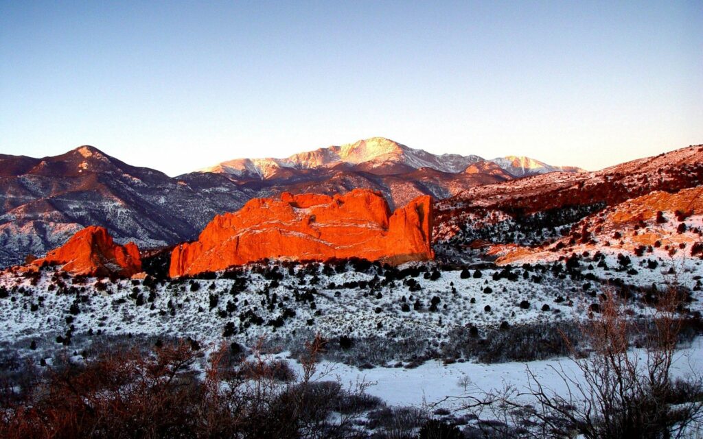 Red rock formations at sunset with snow-capped mountains and green vegetation wallpaper background