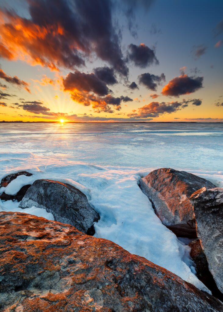 Sunset horizon over icy snow and rugged stones with warm orange and deep blue clouds wallpaper