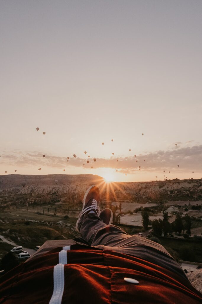 Legs stretched out toward vibrant sunset with hot air balloons over mountains relaxing wallpaper