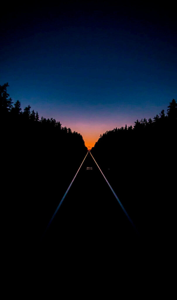 AMOLED wallpaper train tracks fading into golden sunset framed by dark silhouetted forest background