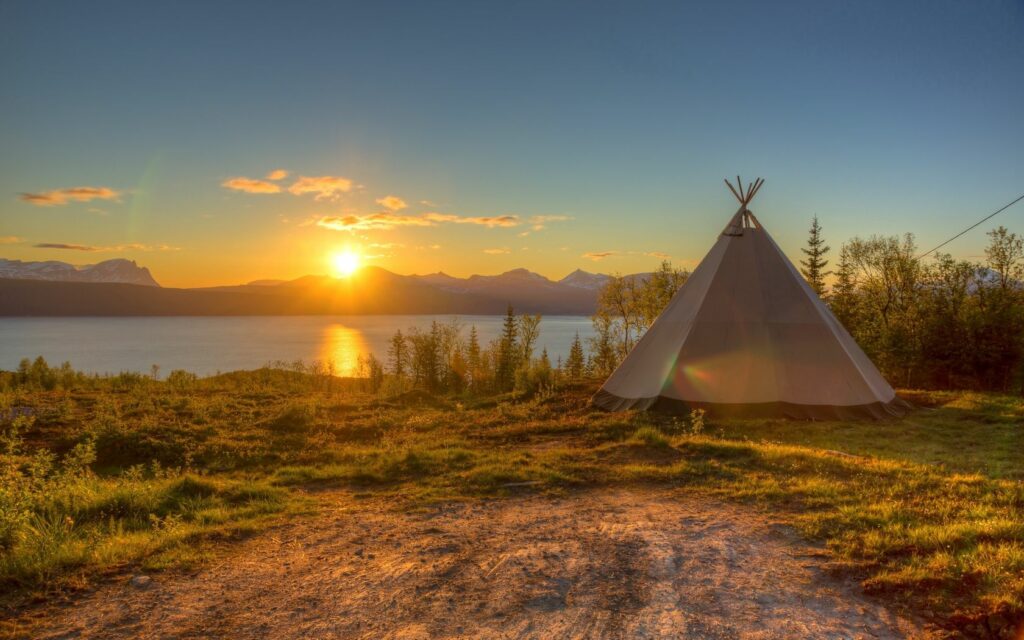 Tranquil tent on grassy lake coast at sunset golden light reflecting serene water wallpaper background