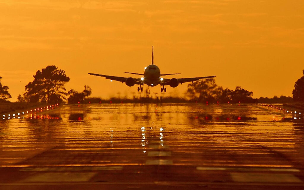 Sunset Touchdown: A Captivating HD Picture of an Airplane Landing on a Rain-Slicked Runway Wallpaper