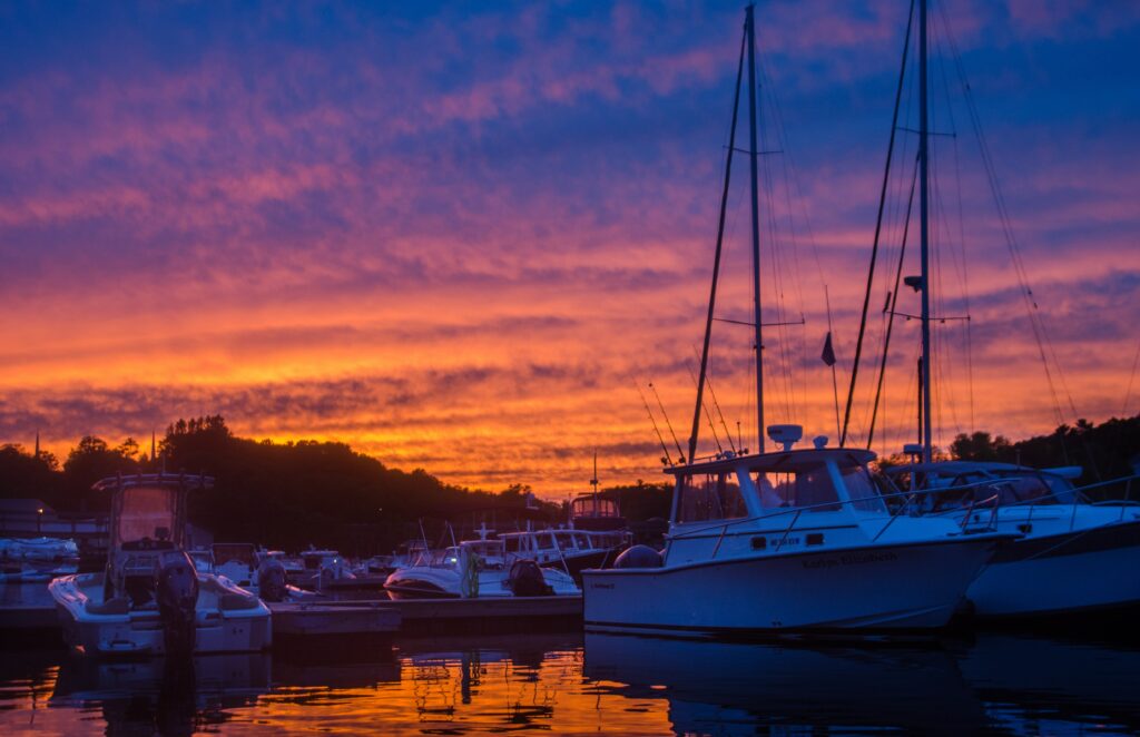 Yachts docked at marina during colorful orange purple sunset reflecting on calm water wallpaper