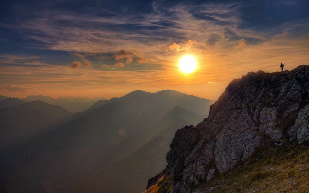 Climber on rugged rock at sunset with golden light over vast mountain landscape wallpaper background