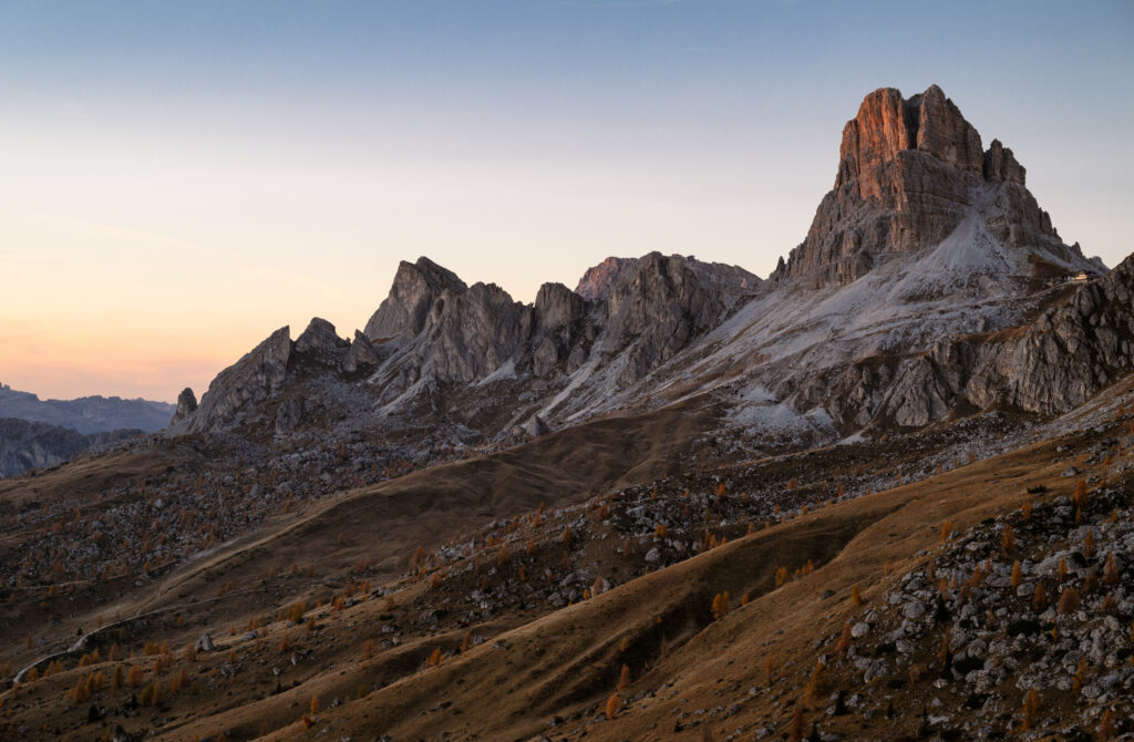 Rugged mountain landscape with rocky peaks and grassy slopes glowing in soft sunset light background Wallpaper
