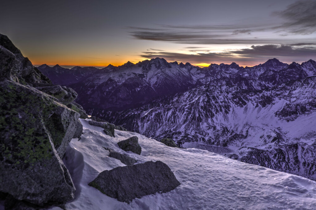 Dramatic mountain landscape at sunset with snow-covered peaks rugged rocks and purple orange sky Wallpaper