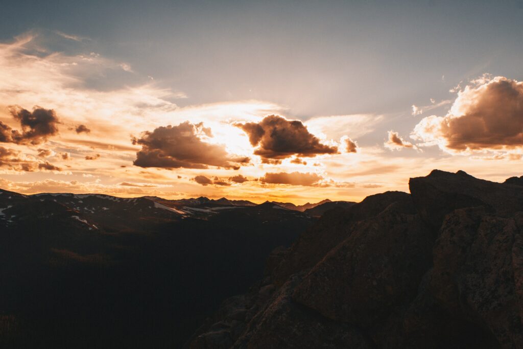Sunset mountain landscape with glowing orange sky dramatic clouds and rugged rocky foreground Wallpaper