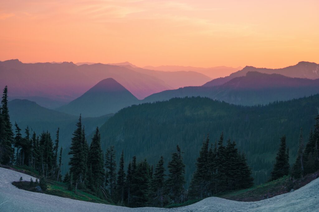 Top view of layered mountain peaks at sunset with vibrant sky and evergreen trees wallpaper background