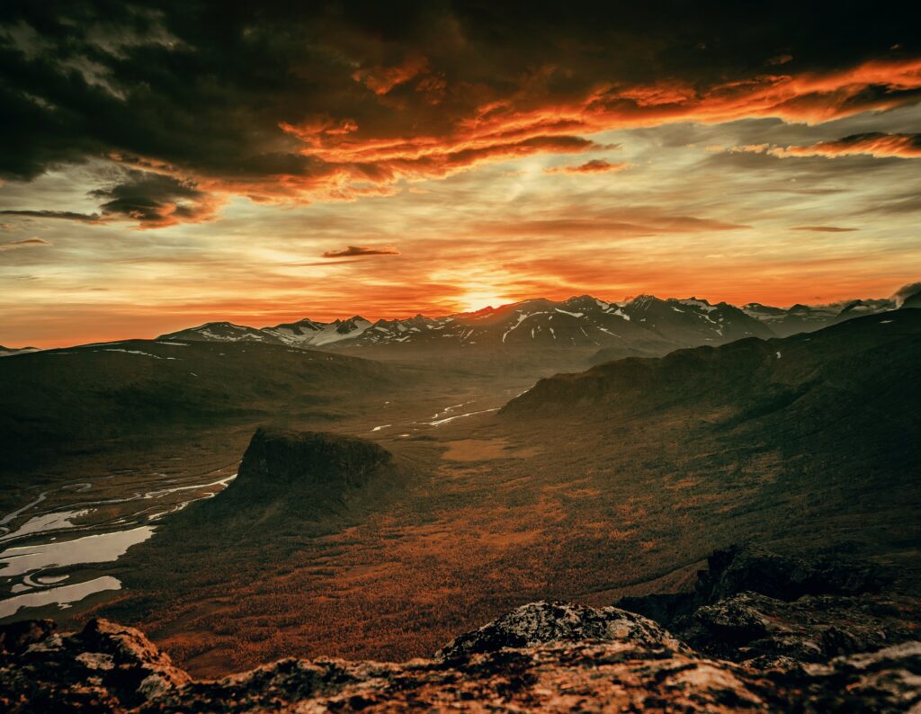 Sunset mountain landscape with rugged terrain and dramatic orange and gold overcast clouds Wallpaper