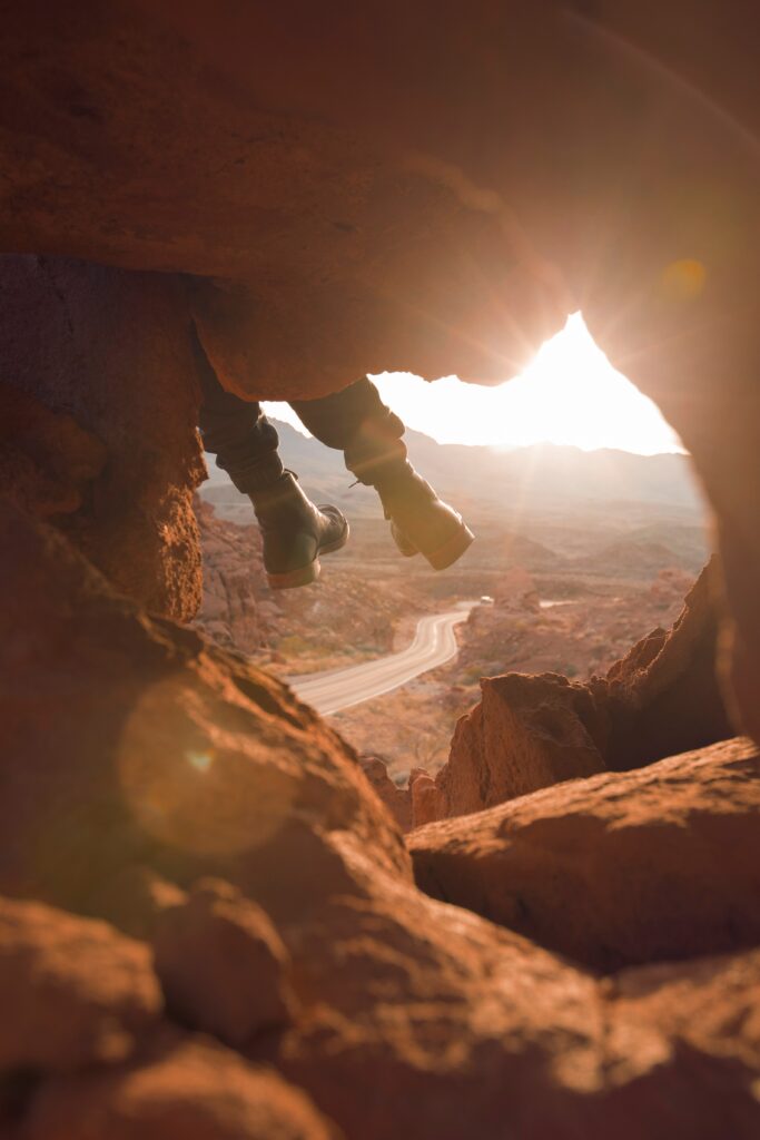 View from rocky cave with boots over edge overlooking winding mountain road at golden sunset Wallpaper