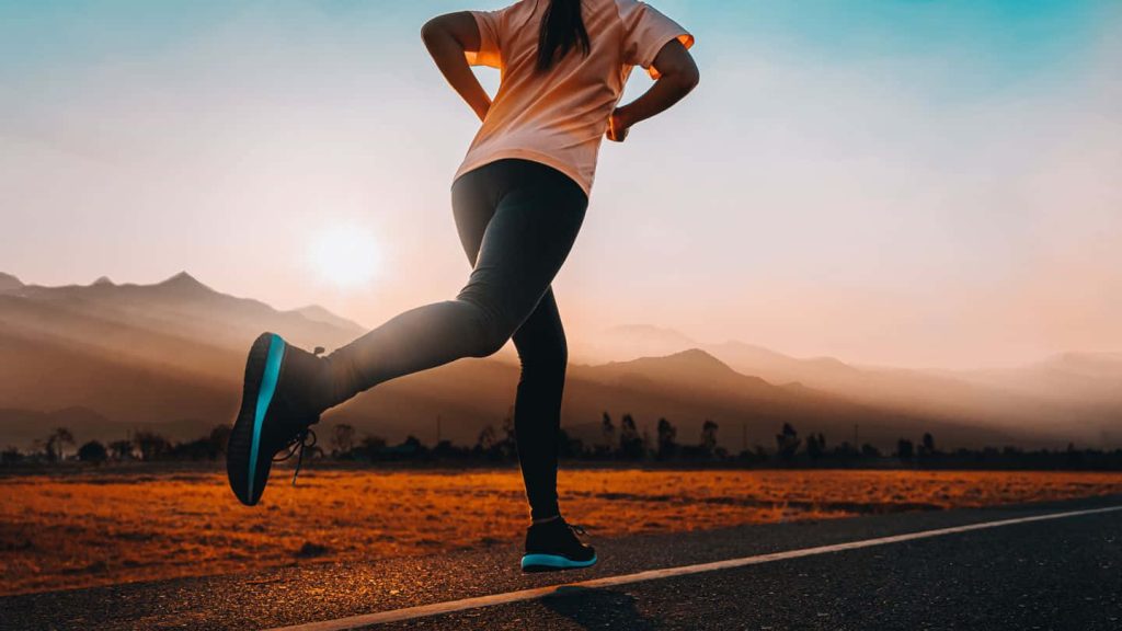 Runner jogging on open road at sunset with mountains in warm golden hour light background Wallpaper