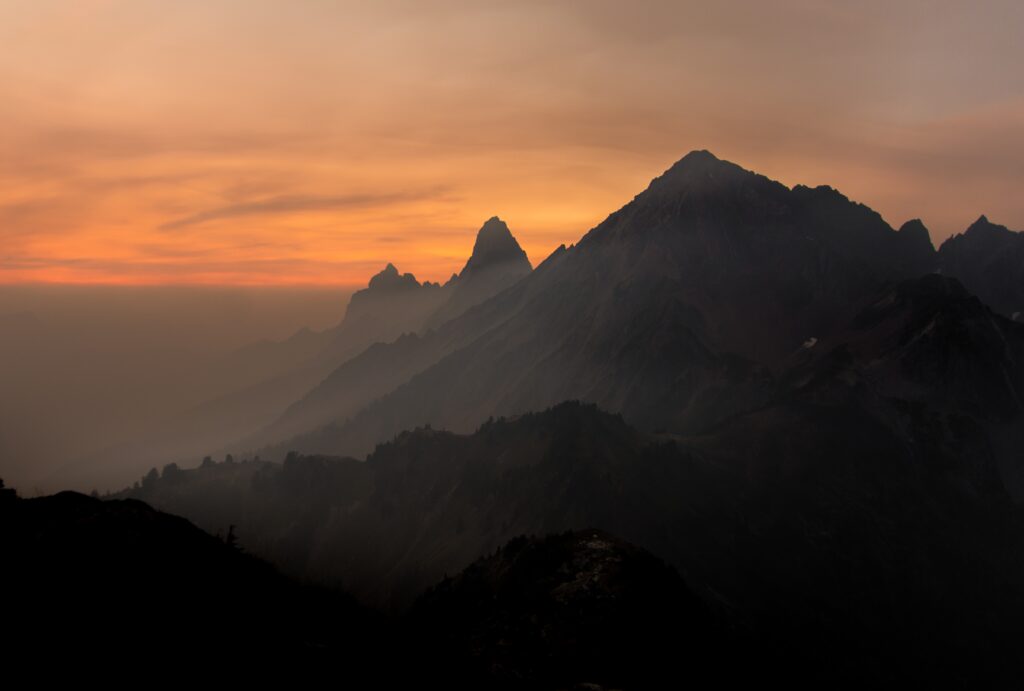 Silhouetted mountain peaks and rugged rocks above rolling fog at warm glowing sunset sky wallpaper background