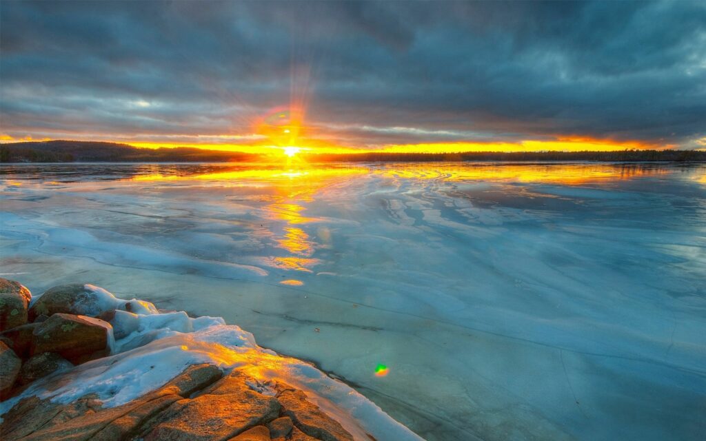 Ocean sunset wallpaper with golden light reflecting on icy water under dramatic clouds