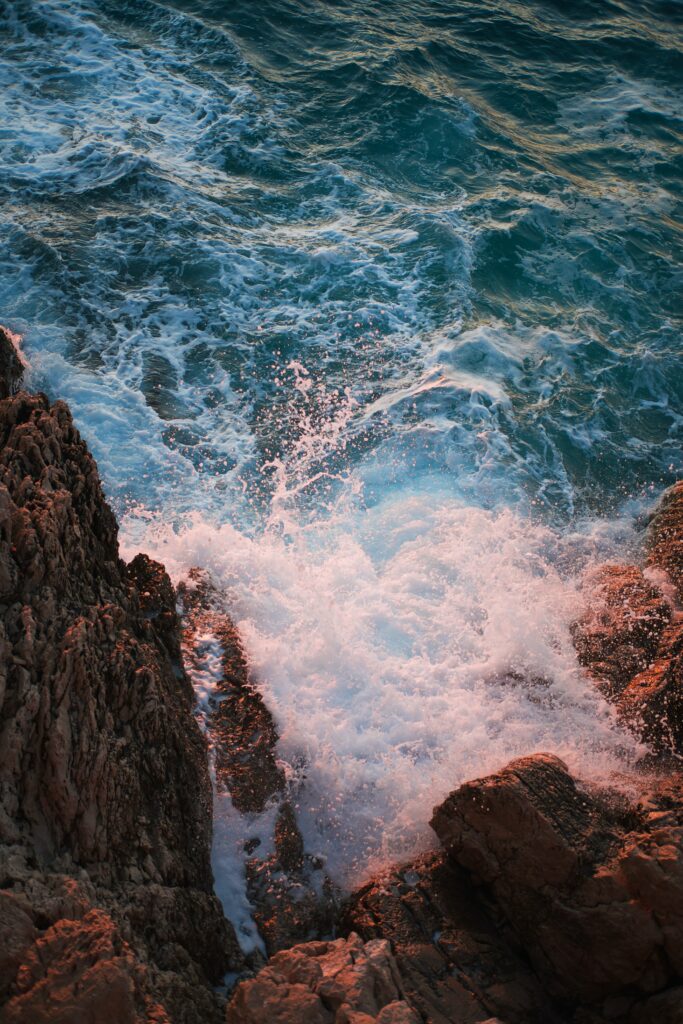 Vivid sunset waves crashing on rugged rocks with sea spray and rich blue ocean textures wallpaper